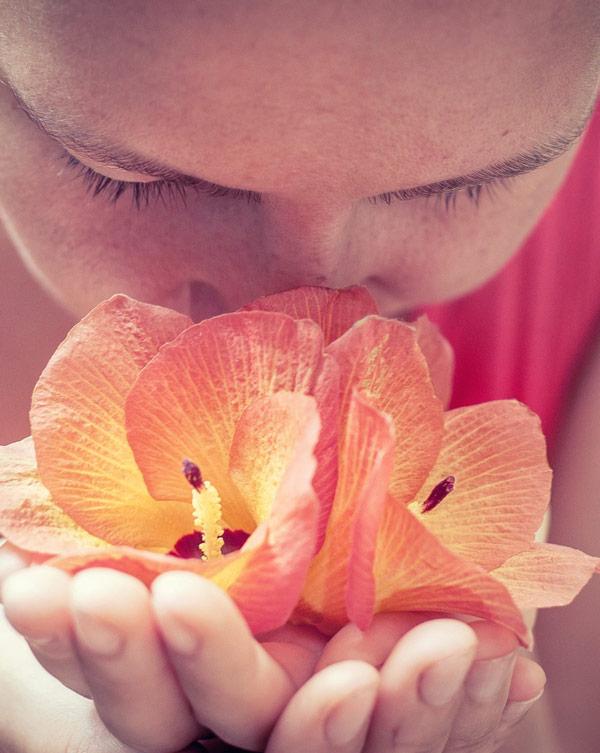 image of woman deeply smelling orange flower